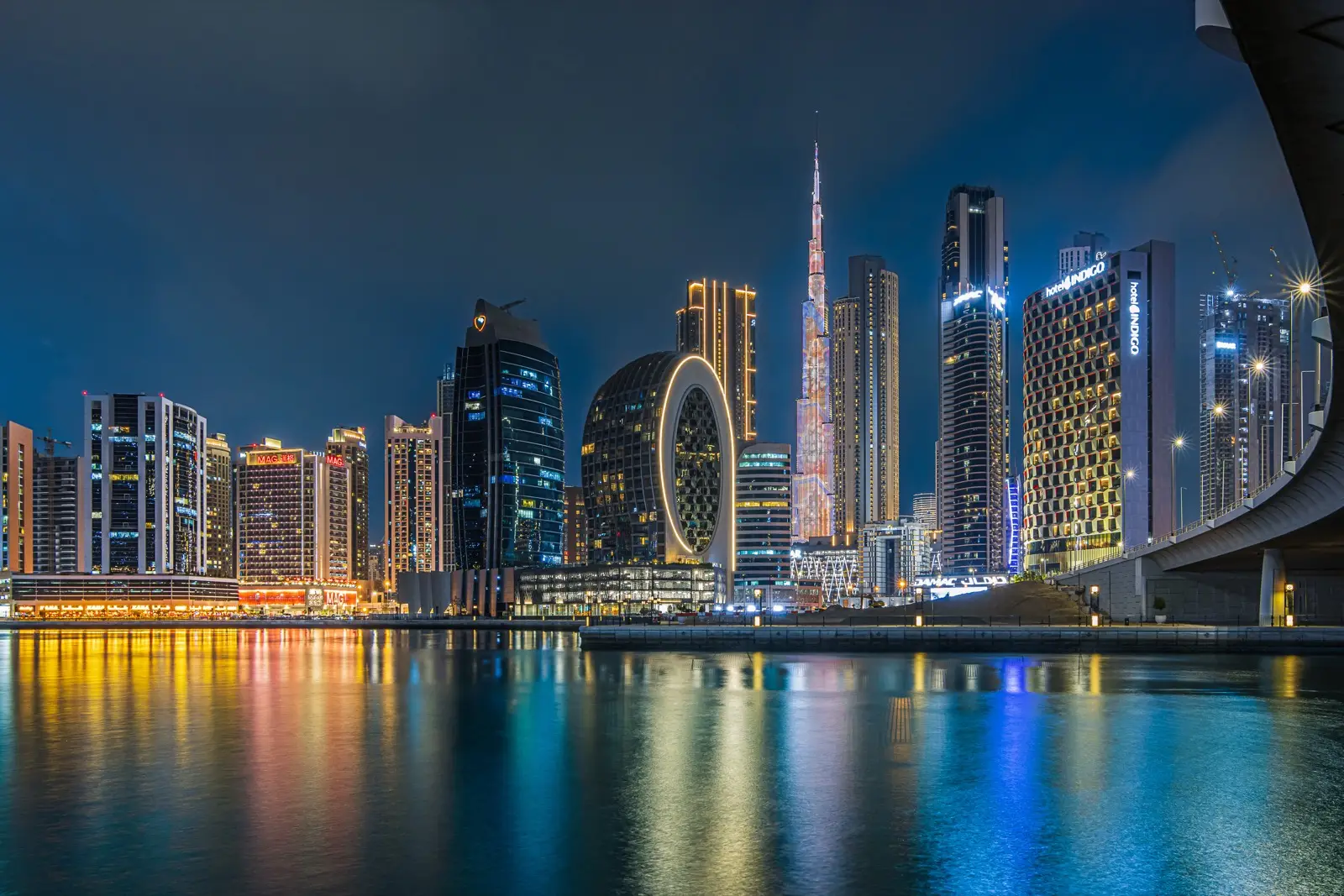 Dubai's Business Bay towers and the Burj Khalifa lit at night above still water, home to one of the world's fastest-growing financial centres