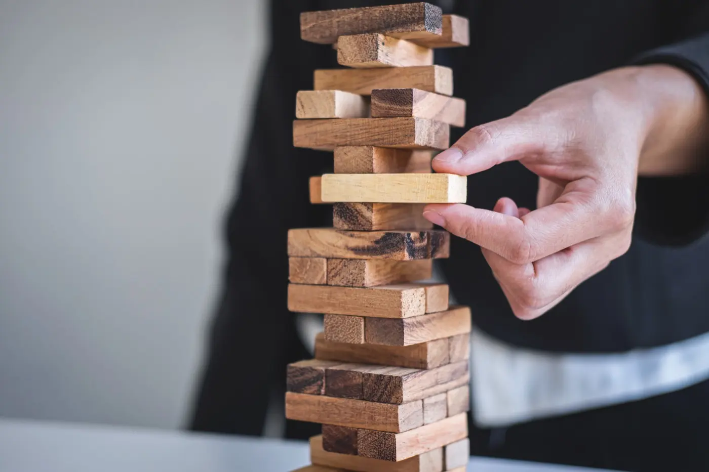 A hand drawing one block from a stacked tower, the test of what a structure can manage without