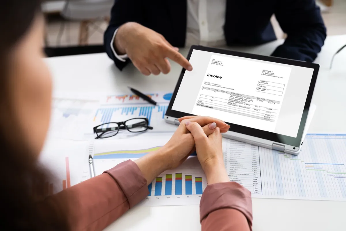 An invoice reviewed on a tablet against printed reports, the records e-invoicing will replace